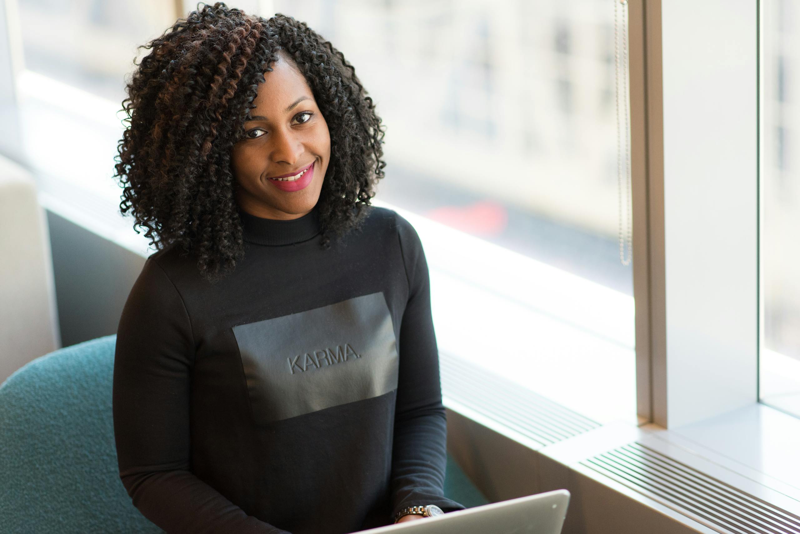 Black woman with curly hair working remotely indoors, exuding confidence and style.
