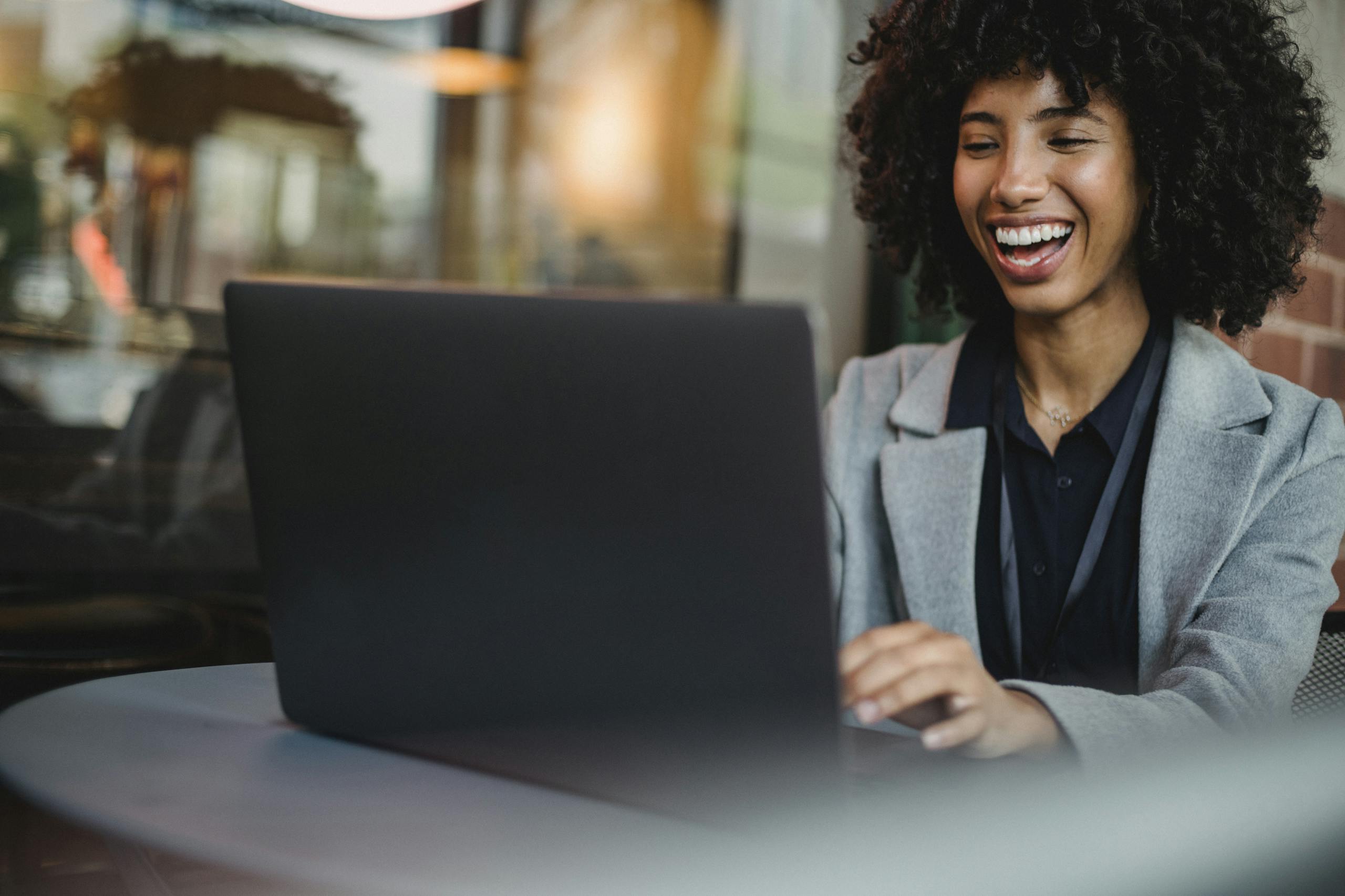 Happy woman in a café, working on a laptop and laughing. Perfect for lifestyle and business themes.