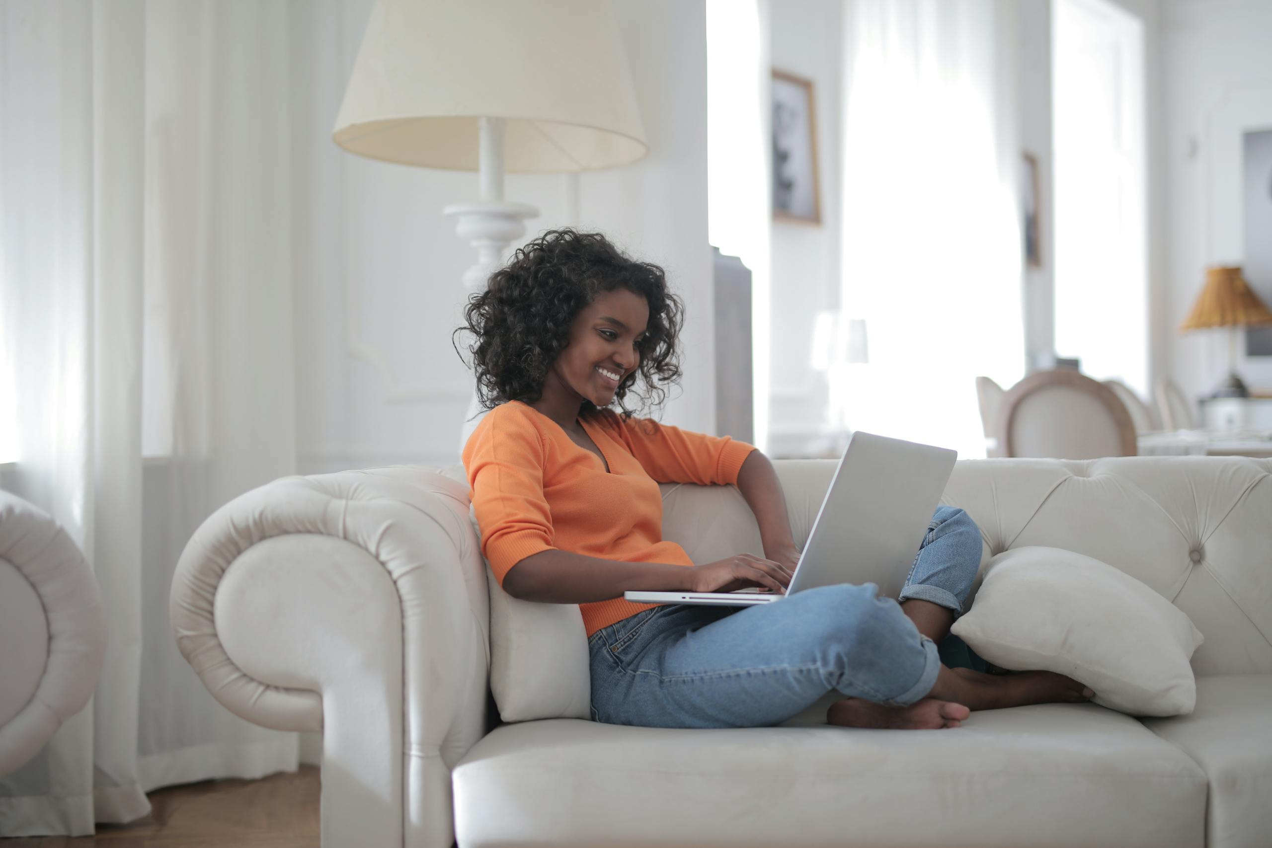 A woman comfortably working from home on a laptop while sitting on a cozy couch.