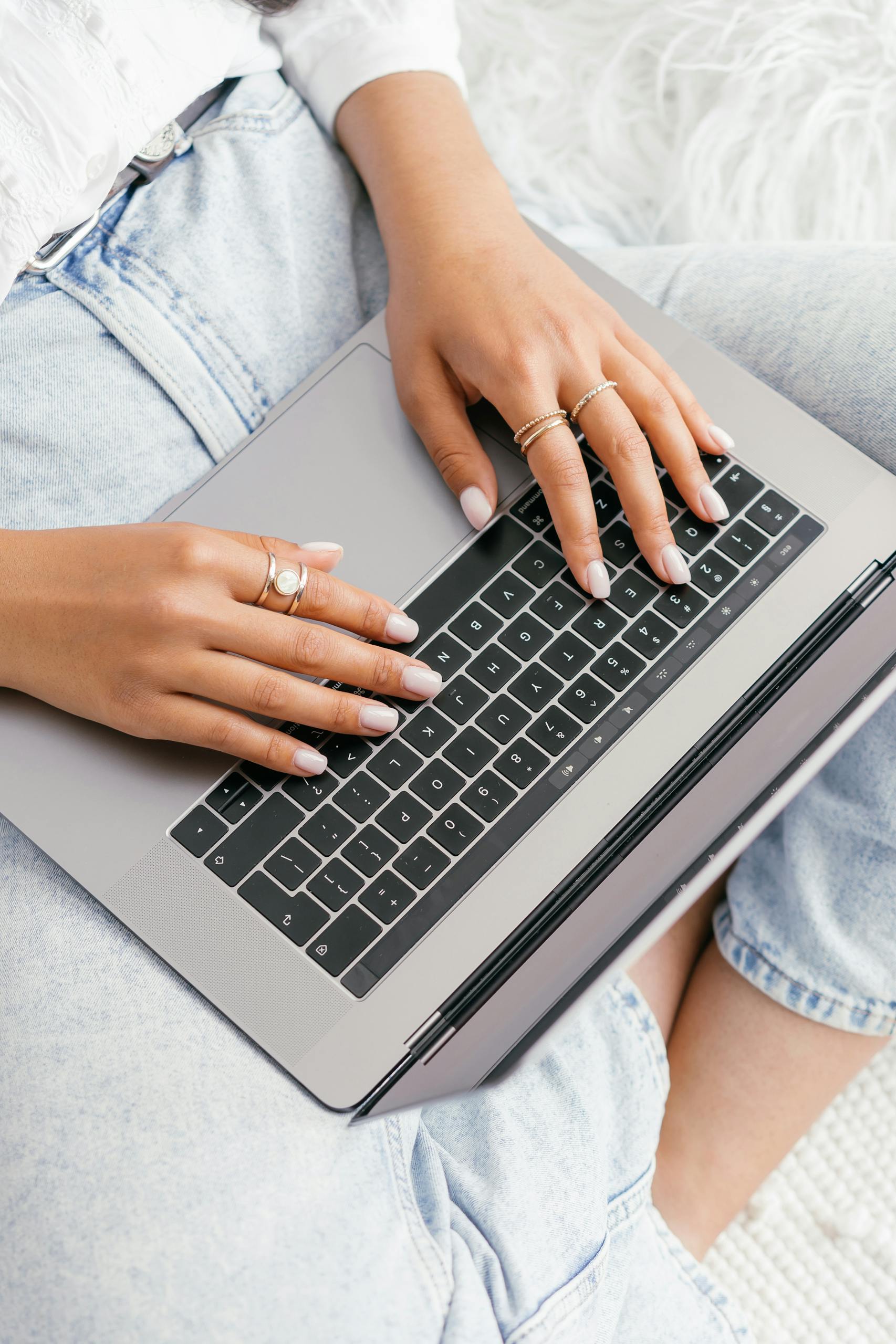 A woman with manicured nails types on a laptop, showcasing modern technology.