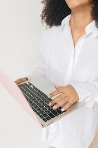 Close-up of woman holding laptop against a soft white background.