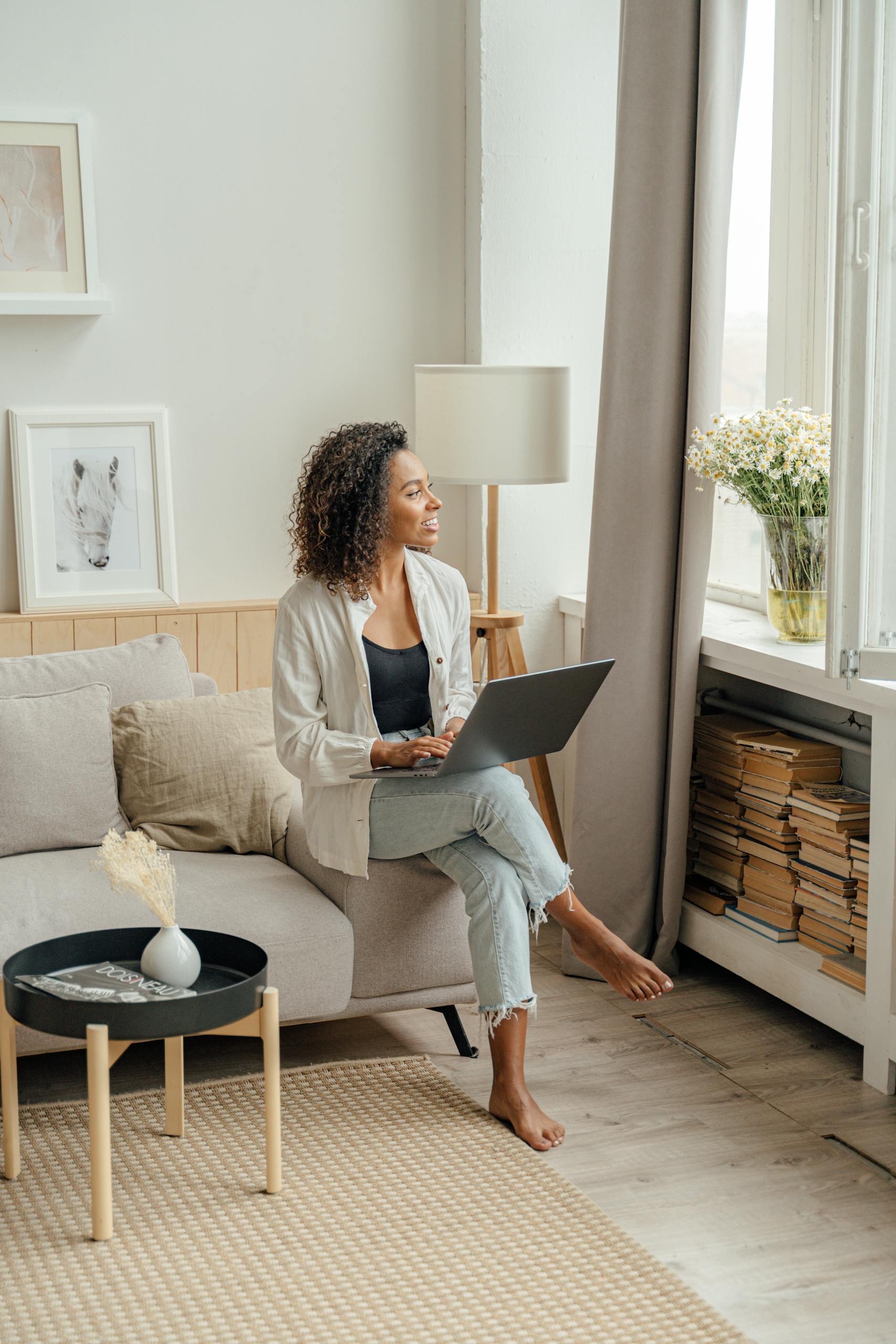 African American woman working on laptop at home, enjoying natural light by the window.