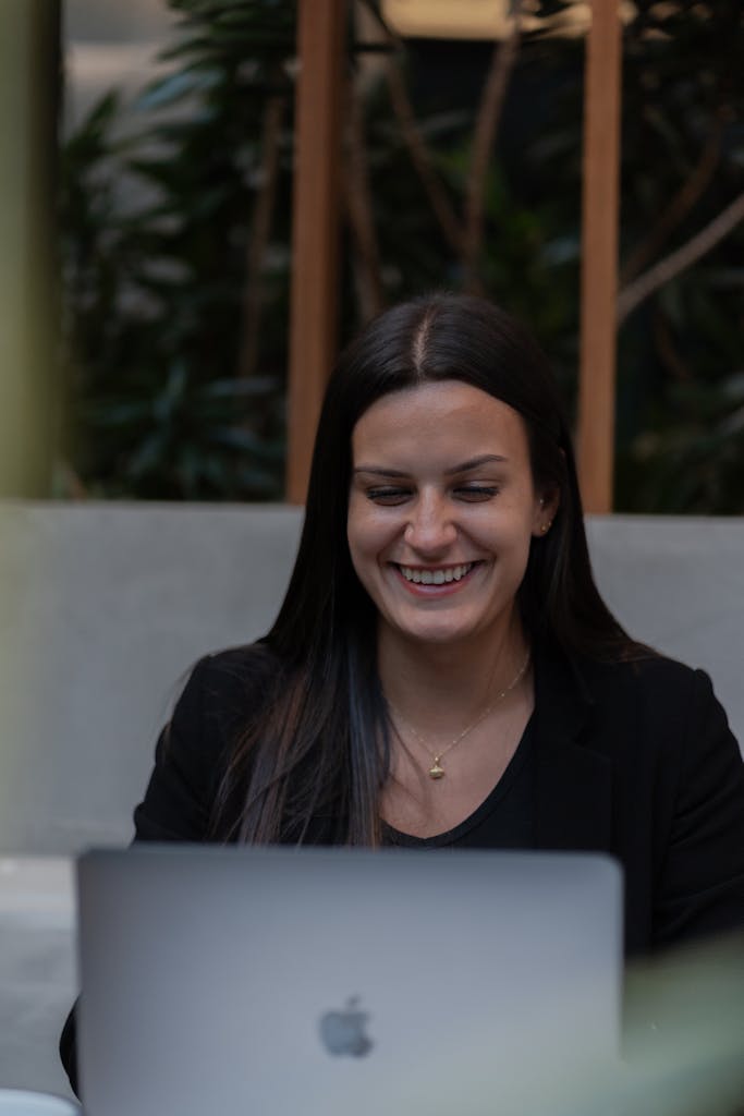 Smiling woman working on a laptop indoors, surrounded by plants, conveying a positive work environment.