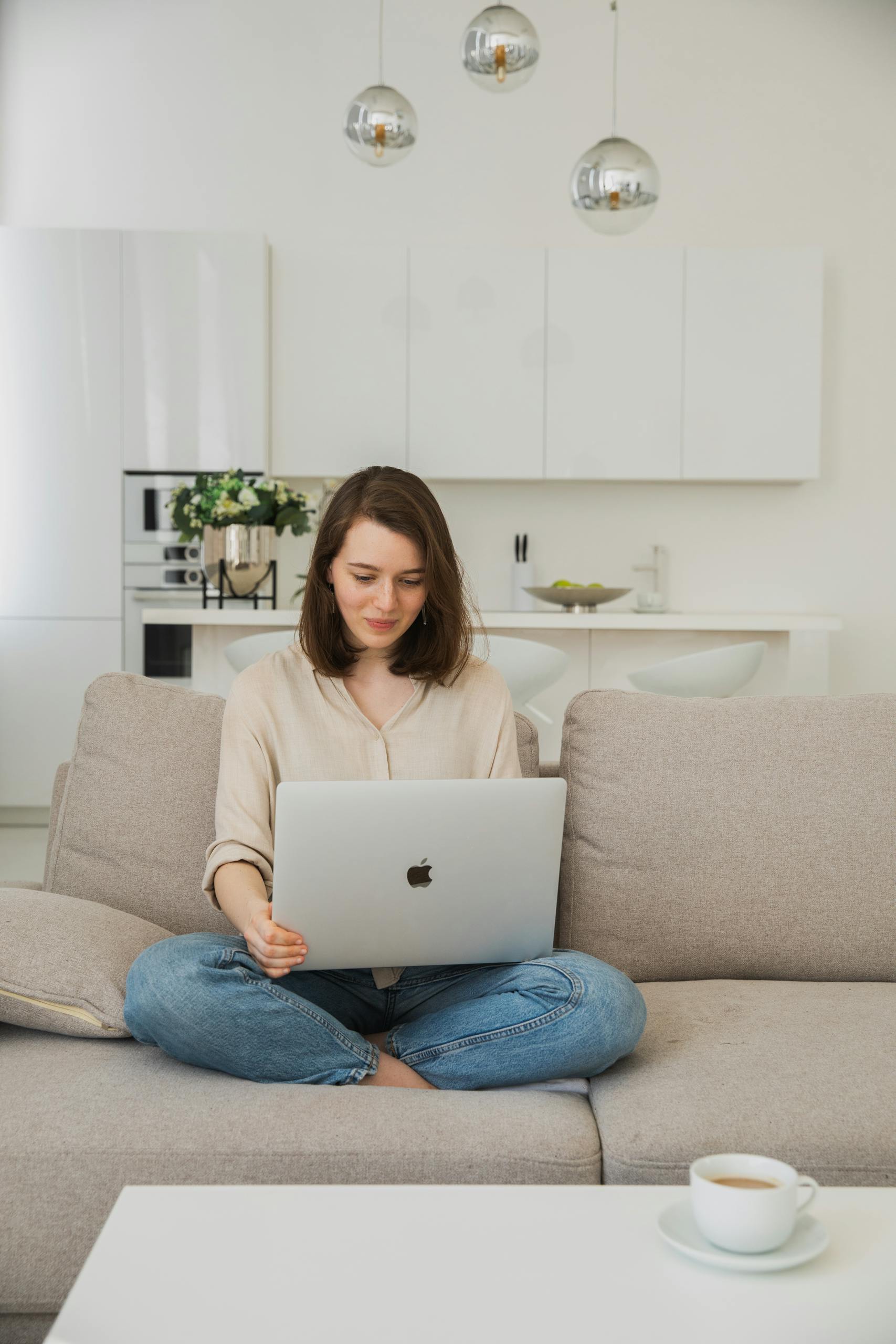 Young woman comfortably using a laptop on her sofa in a bright living room.
