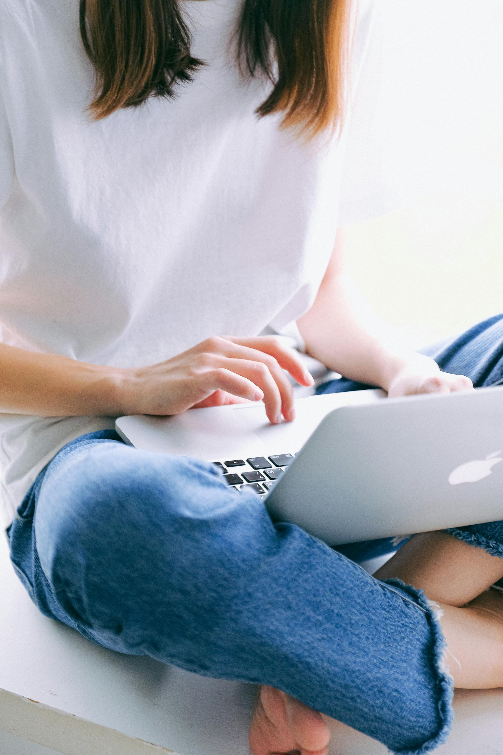 A woman wearing casual clothes works on a laptop while seated comfortably indoors.