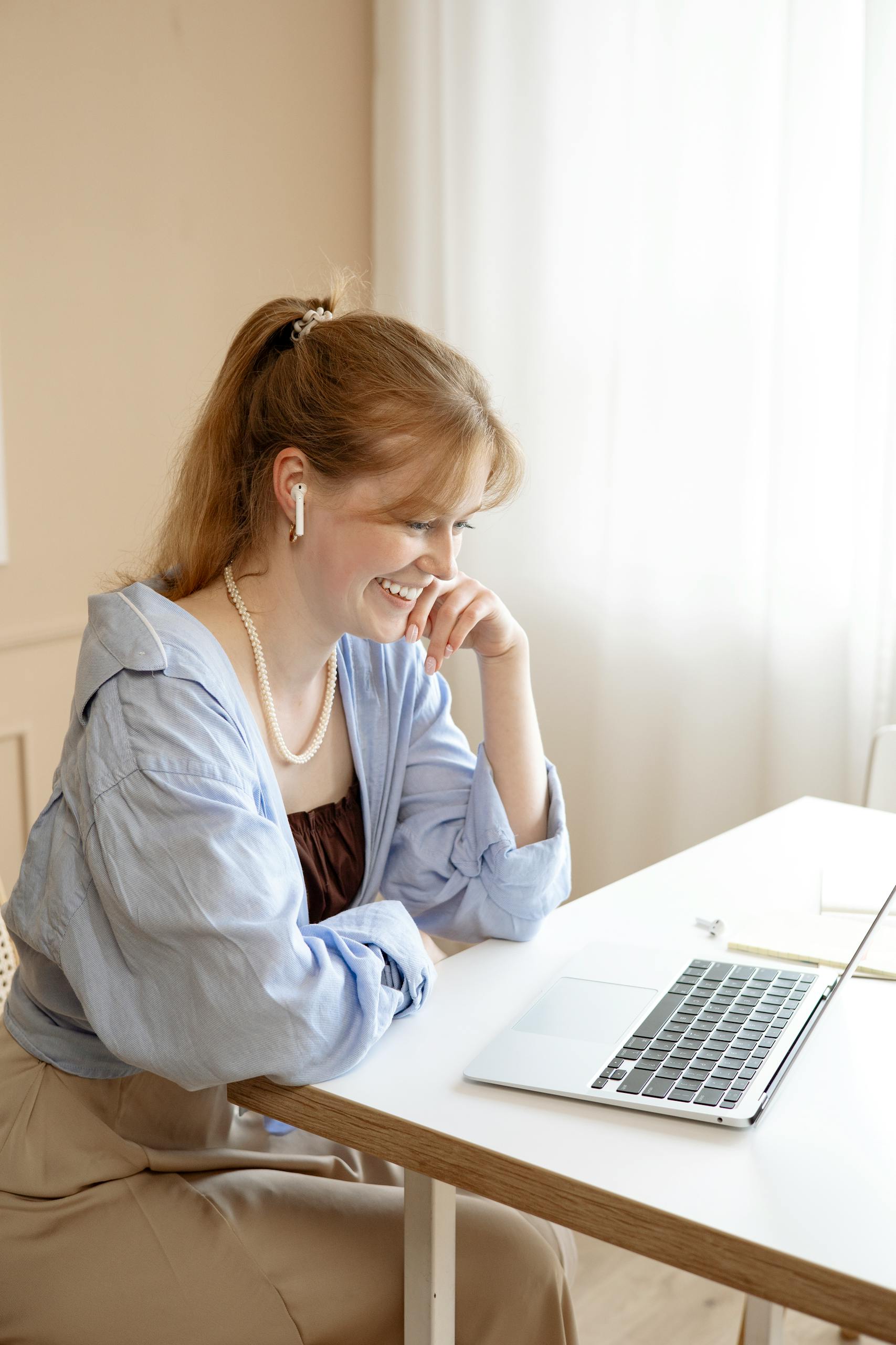 Smiling woman using a laptop at home, dressed casually, with natural lighting. Perfect for lifestyle or remote work themes.