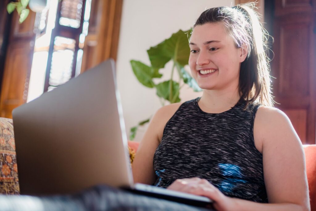A smiling woman in a comfortable home setting using her laptop for work or leisure.